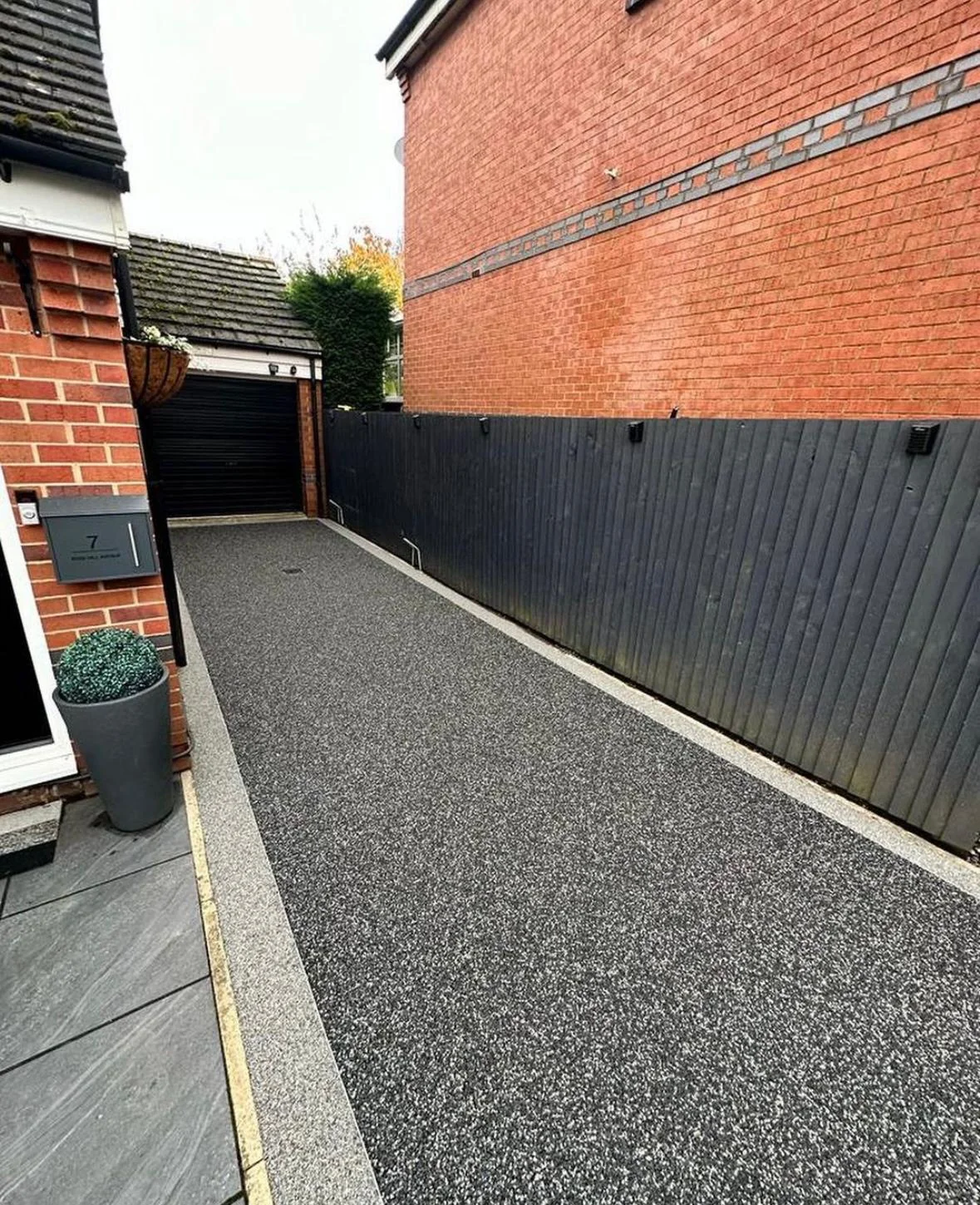 Dark resin side walkway between a brick house and boundary fence