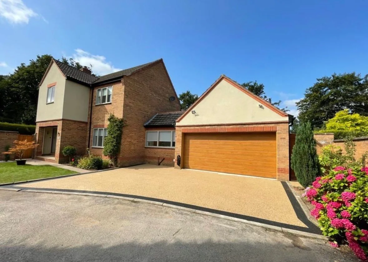 Golden resin driveway in front of a detached garage and planted border
